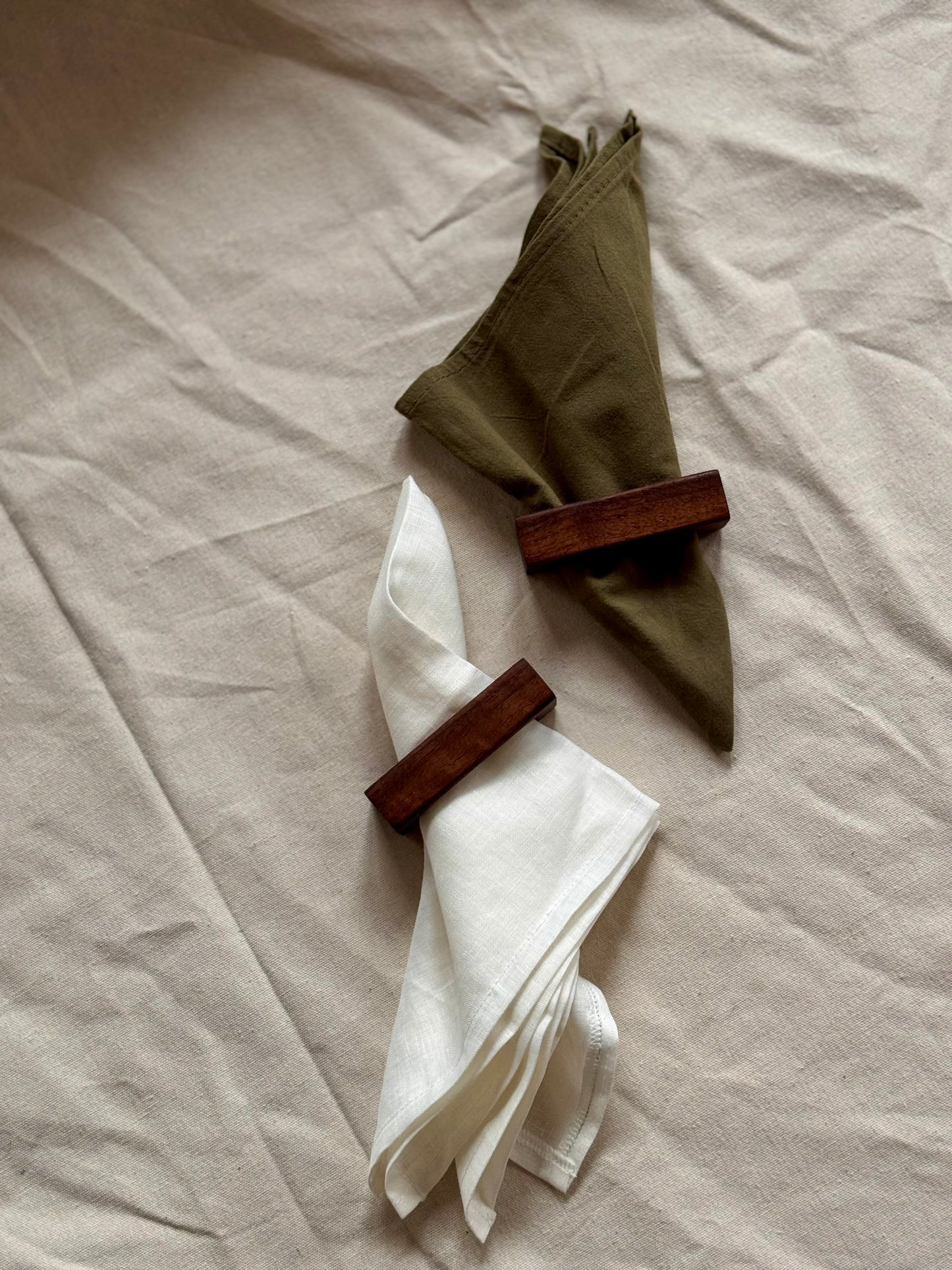 Two wooden napkin rings holding white and green napkins on a beige fabric background