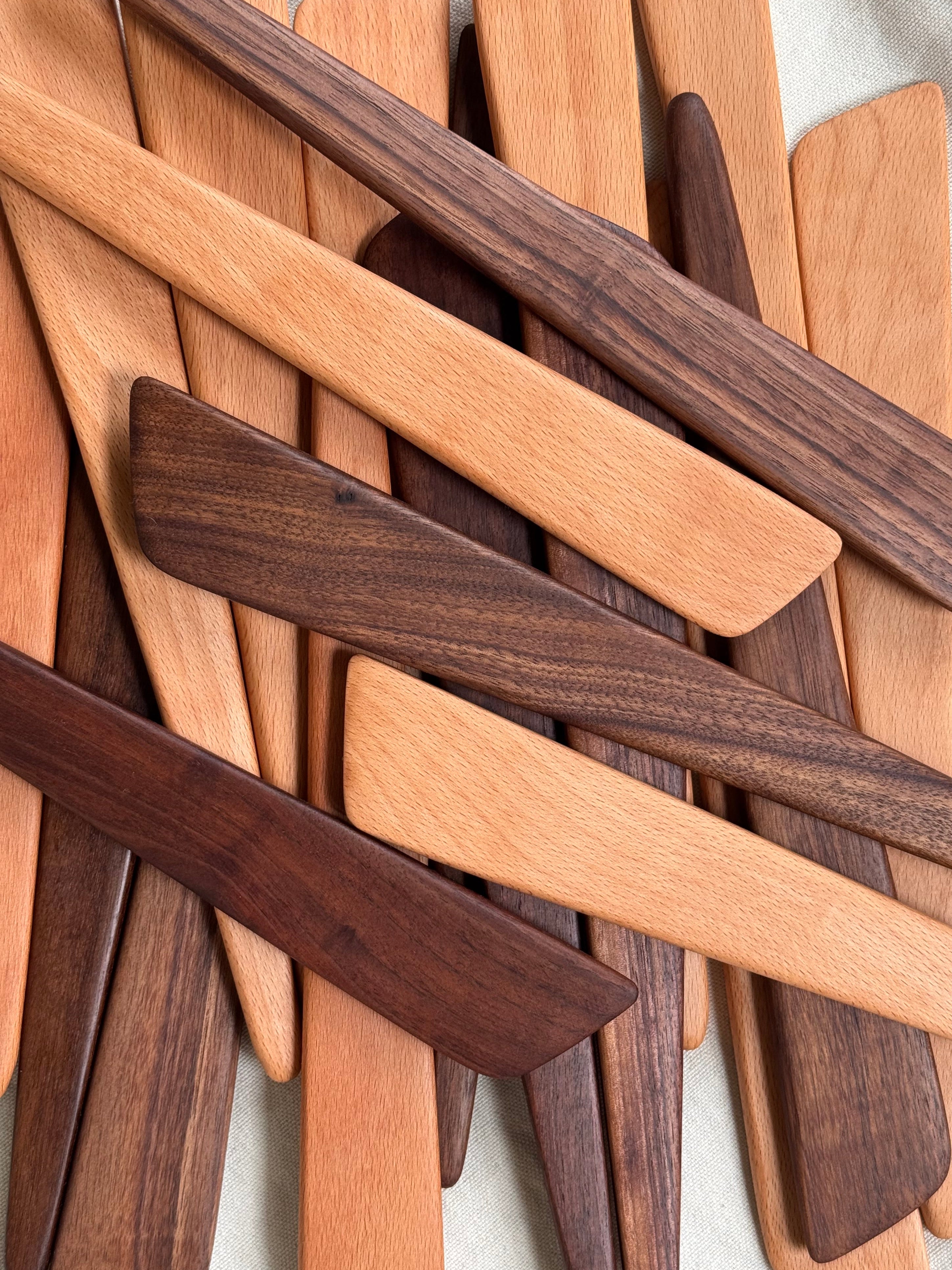 Stack of wooden spatulas in various shades of brown on a light background