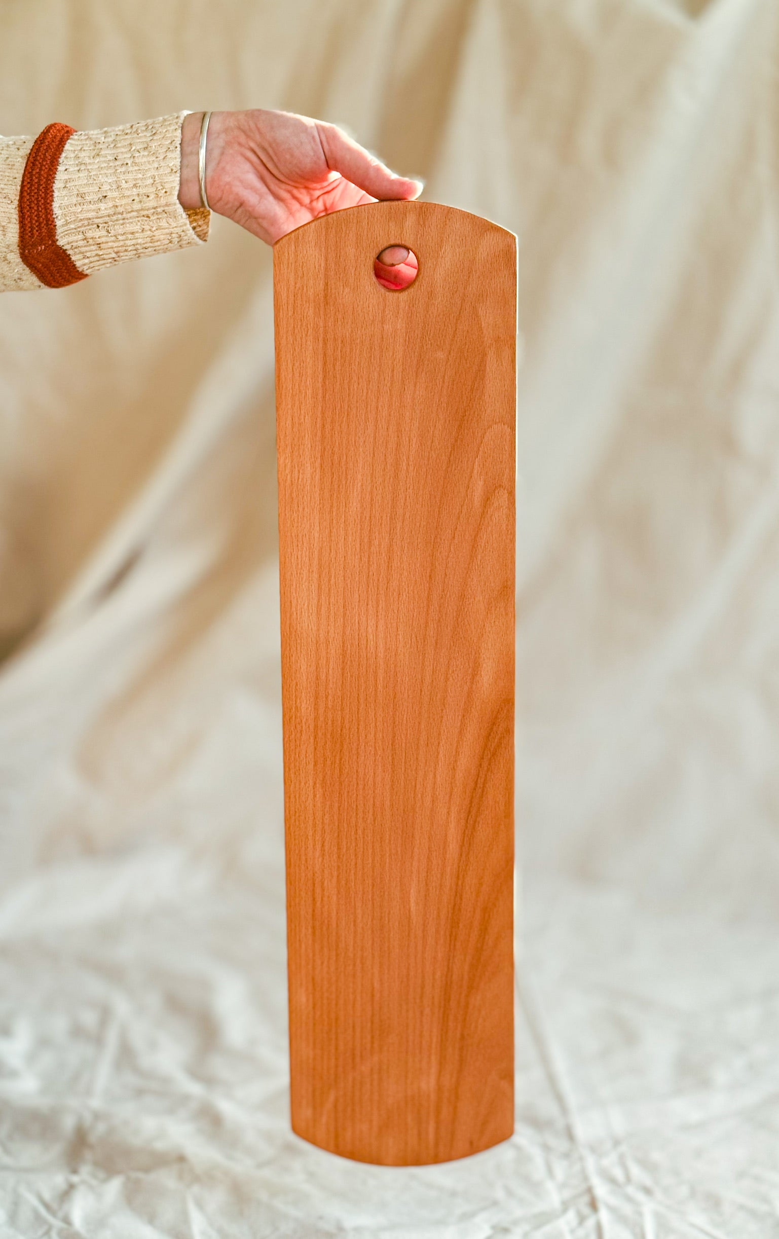 Wooden beech cutting board held by a person against a beige background