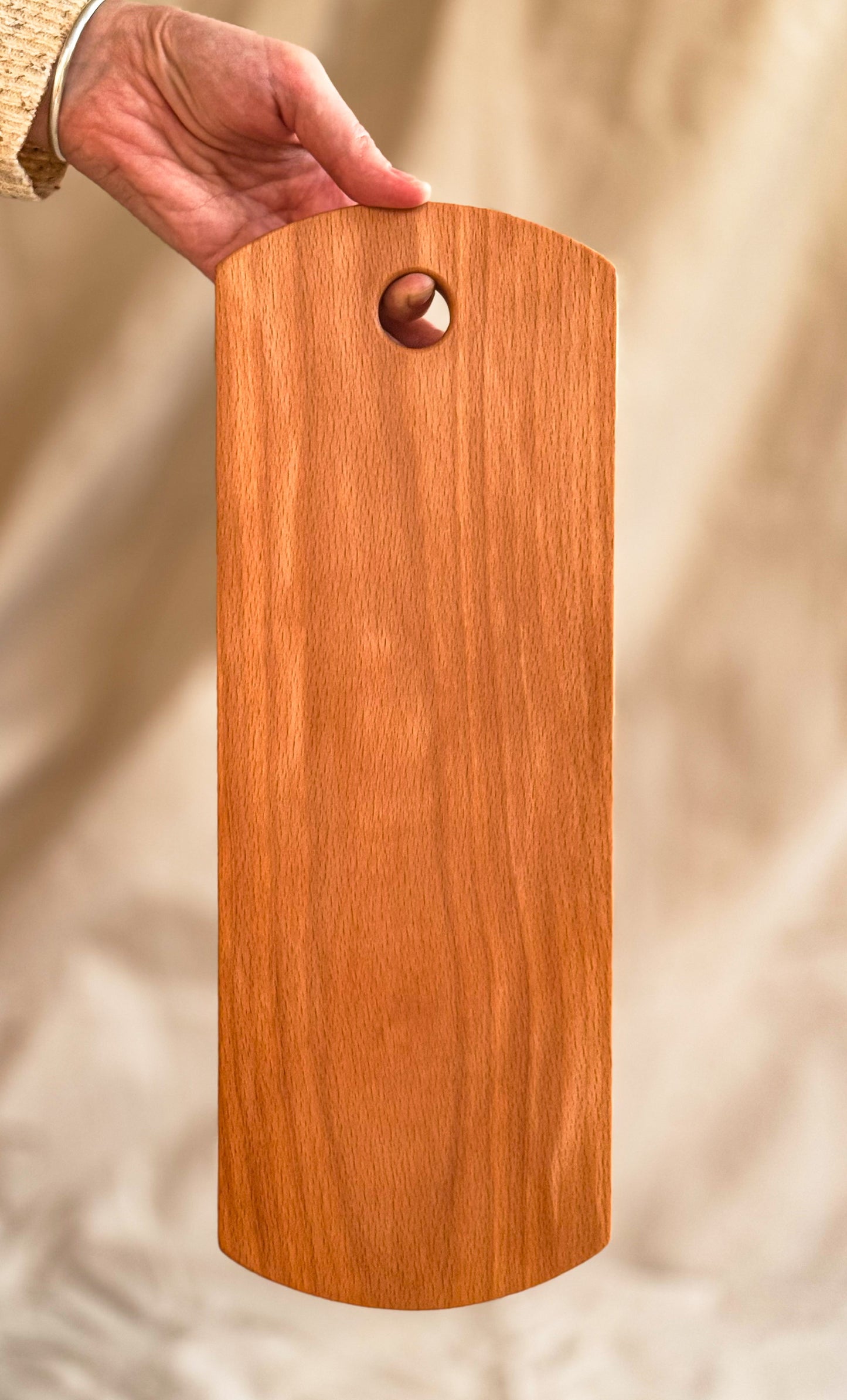 Wooden cutting board held by a hand against a neutral background