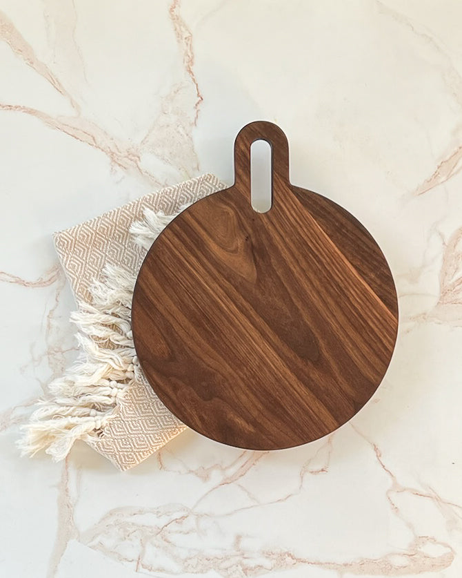 Handmade modern looking dark wooden circular round charcuterie/cutting board with rounded handle made by Camino Woodshop in Milwaukee, WI
